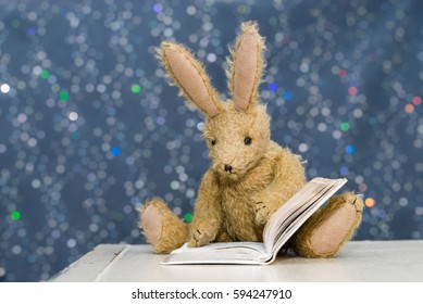 Cute toy rabbit with long ears reading a book. Blue bokeh background. Storytime, child's reading concept.