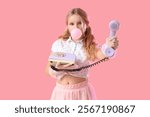 Cute trendy girl with retro phone blowing bubble gum on pink background