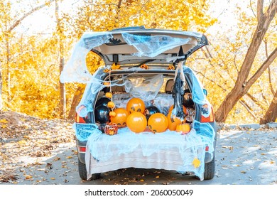 cute trunk of car decorated for Halloween with cobwebs, orange balloons, pumpkins and sweets, the outdoor creative activity concept in autumn in October