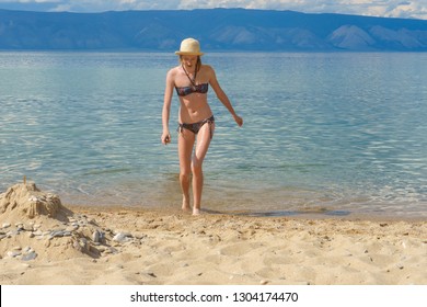 Cute Tween Girl In Hat And Bikini Getting Out Of Water After Swimming In Lake Baikal In Summer Sunny Day. Beautiful Young Lady Relaxing At Beach. Summer Vacation, Outdoor Recreation Concept