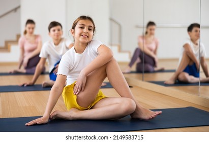 Cute tween girl performing seated twisting asana Matsyendrasana during yoga class with sporty family in fitness studio..