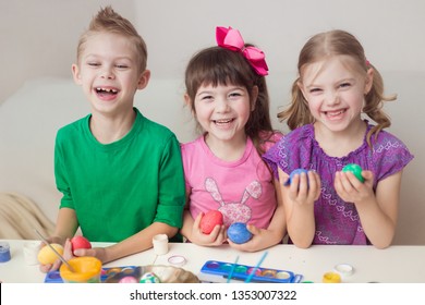 Cute Twin Triplets Children, First Graders, Painted Easter Eggs And Looking At The Camera, Smiling