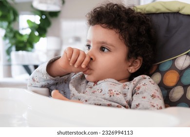 Cute two year old baby girl sitting on a high chair sucking her thumb in a home setting - Powered by Shutterstock