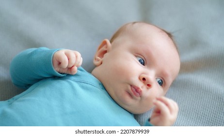 Cute Two-month-old Baby In Blue Clothes Looks Into Camera. Sweet Newborn Boy Lies On The Sofa. Shooting From The Upper Angle Of A Chubby Male Kid. Beautiful Infant Boy With Blue Eyes. 