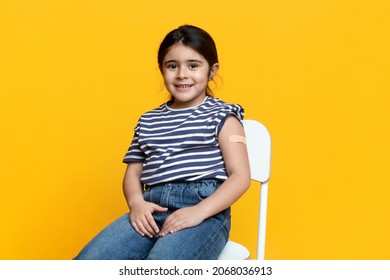Cute Vaccinated Little Girl Showing Arm With Adhesive Bandage After Injection Shot, Smiling Preteen Female Child Posing On Yellow Background After Getting Coronavirus Vaccination, Copy Space