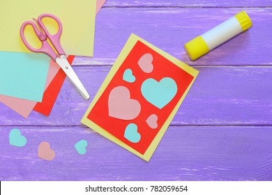 Cute Valentines Day Card Made From Colored Paper. Scissirs, Glue Stick, Colored Paper Sheets On A Wooden Table. Valentines Day Paper Crafts For Kids. Top View