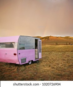 cute vintage camper trailer in the sawtooth mountain range in a desolate camp ground during a summer rain storm with a rainbow in the distance toned with a retro vintage instagram filter 