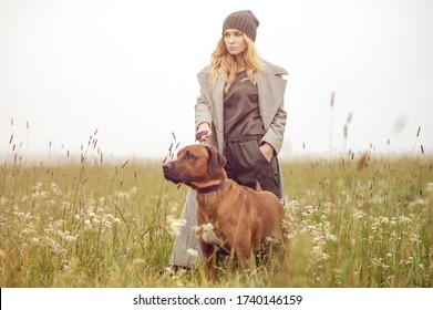 Cute Well Dressed Pretty Young Caucasian Blonde Hair Adult Teenage Girl In Fashion Dress Coat Outdoor With A Dog At Mist Countryside Landscape Field Spring Or Autumn Weather Depressed Mood