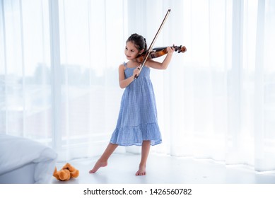 A cute white Asian girl wearing a blue skirt dress is playing a violin in a white background with sunlight. - Powered by Shutterstock