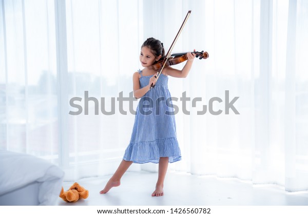 青いスカートドレスを着たかわいいアジア人の女の子が 日差しのある白い背景にバイオリンを弾いている の写真素材 今すぐ編集