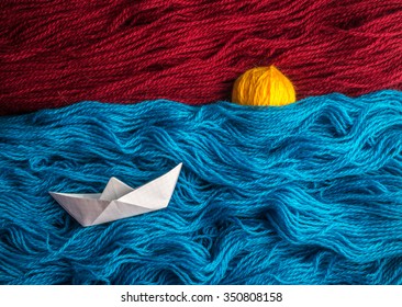 Cute White Of Origami Boat Floating On The Waves Of Woolen Yarn, On The Horizon The Sun Goes Down That Is Made Of A Coil Thread