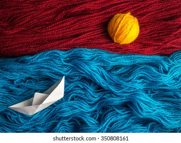 Cute White Of Origami Boat Floating On The Waves Of Woolen Yarn, On The Horizon The Sun Goes Down That Is Made Of A Coil Thread