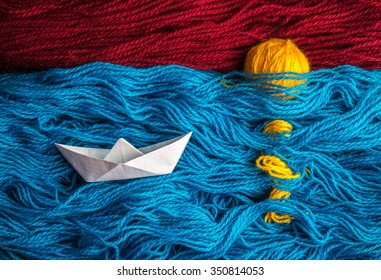 Cute White Of Origami Boat Floating On The Waves Of Woolen Yarn To The Sunset, Where Are Visible On A Surface Of Rays Of The Sun