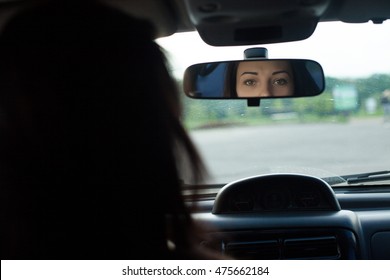 Cute Woman With Beautiful Eyes Is Looking In Rearview Mirror In A Black Car.