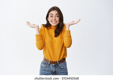 Cute Woman Dont Know Anything, Raising Hands Up And Shrugging With Silly Smile, Have No Idea, Say Sorry For Being Unaware, Standing Against White Background.