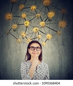 Cute woman in glasses with many ideas light bulbs above head looking up isolated on wall background. 