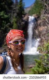 Cute Woman Hiker With Braided Hair Wearing A Tank Top Poses At Running Eagle Falls Waterfall In Glacier National Park