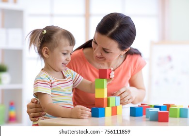 Cute woman and kid girl playing educational toys at kindergarten or nursery room