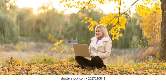 Cute Woman With Laptop In The Autumn Park. Beauty Nature Scene With Colorful Foliage Background, Yellow Trees And Leaves At Fall Season. Autumn Outdoor Lifestyle. Happy Smiling Woman On Fall Leaves