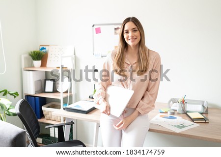 Cute woman working as an administrative assistant holding a laptop computer in an office and looking ready to work
