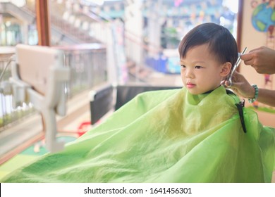 Cute worried little Asian 3 - 4 years old toddler boy child getting a haircut while watching cartoon on smartphone in modern hairdresser's barber shop at department store in Bangkok Thailand - Powered by Shutterstock