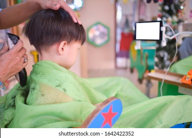 Cute worried little Asian 3 - 4 years old toddler boy child getting a haircut while watching cartoon on smartphone in modern hairdresser's barber shop at department store in Bangkok Thailand - Powered by Shutterstock