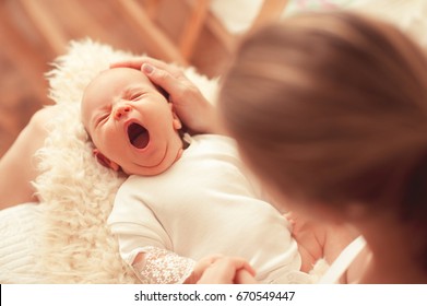 Cute yawning infant baby on mothers hands in room. Motherhood. Maternity. Childhood. 