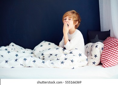 Cute Yawning Kid In Pajamas Sitting In Bed