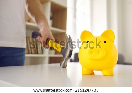 Cute yellow ceramic piggy bank about to be smashed with a hammer. Man in dire need of money is going to break his piggybank on the table. Cropped close up shot. Saving up, or being in debt concepts
