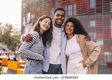 Cute young african guy is hugging his interracial girlfriends posing for camera. Friends wear casual clothes for walk. Happy weekend concept.