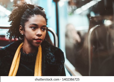 A cute young African-American female on a seat of metro in a demi-season coat and yellow scarf is thoughtfully looking into the window of a subway carriage, with a copy space area on the right - Powered by Shutterstock