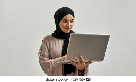 Cute young arabian woman in hijab looking into laptop screen while posing on light background, widescreen. Beautiful muslim lady - Powered by Shutterstock