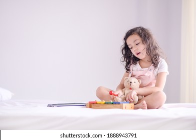 A cute young Asian girl was happily playing a wooden toy instrument in the bedroom - Powered by Shutterstock