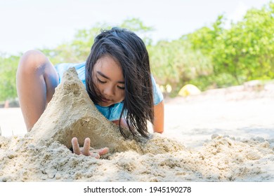 A Cute Young Asian Girl Sitting And Playing Alone On A Sandy Beach, Having Fun, Building A Sand Castle.