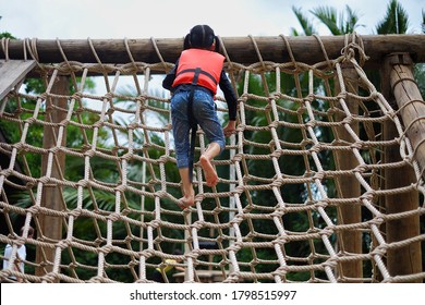 A cute young Asian girl wearing orange life vest is going up a climbing net in an obstacle course at a summer camp.  - Powered by Shutterstock