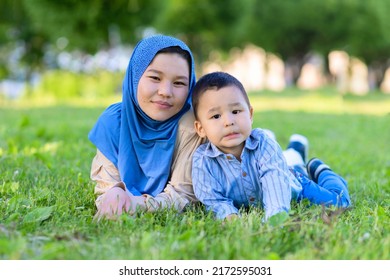 Cute young asian islamic woman in hijab, headscarf lying on the grass with child, pastime leisure with son. Portrait happy muslim Kazakh mother with kid on grass