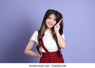 The Cute Young Asian Woman With Preppy Dressed Standing On The Purple Background.