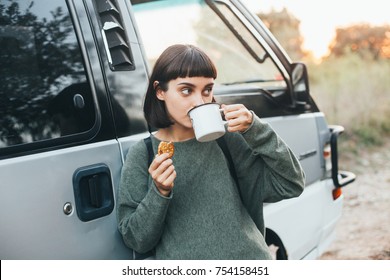 Cute Young Attractive Female Tourist Drinks Coffee Or Hot Tea During Rest Stop In Forest On Hiking Trip On Road, Leans On Camper Van And Snacks On Tasty Cookie, Concept Camping And Travel Cup Mockup