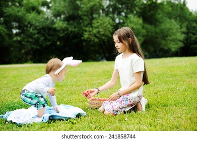 Cute young baby  brother and school aged sister playing with Easter eggs outside in the park together.