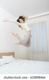Cute young beautiful girl at morning jumping on the bed