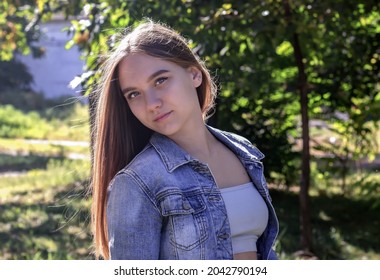 cute young beautiful teenage girl with long brown hair stands in the park against a background of green trees, her head thrown back