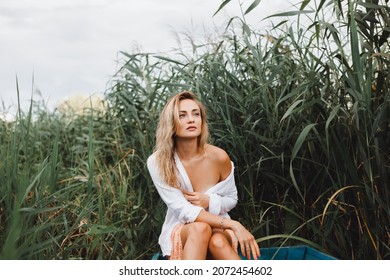 Cute young blonde woman in a skirt and white shirt is resting in a wooden boat on the lake on a sunny warm day in summer
