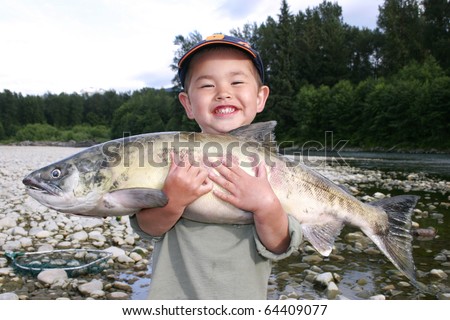 Cute young boy with great smile holding large salmon out fishing on a river