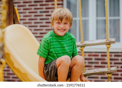 Cute Young Boy In Green Shirt And Black Shorts Is Playing On Back Yard Playground. 