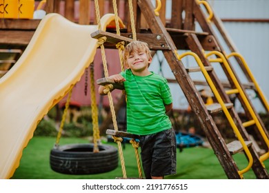 Cute Young Boy In Green Shirt And Black Shorts Is Playing On Back Yard Playground. 