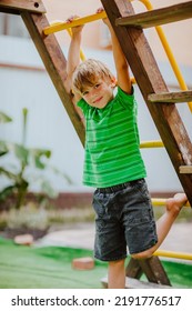 Cute Young Boy In Green Shirt And Black Shorts Is Playing On Back Yard Playground. 