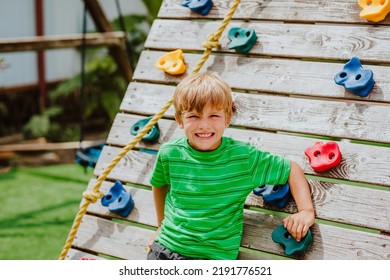 Cute Young Boy In Green Shirt And Black Shorts Is Playing On Back Yard Playground. 