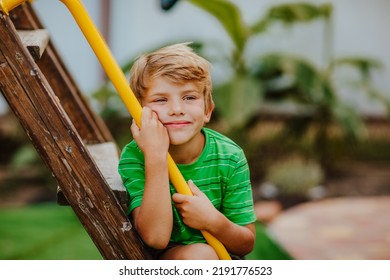 Cute Young Boy In Green Shirt And Black Shorts Is Playing On Back Yard Playground. Copy Space