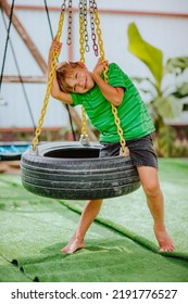 Cute Young Boy In Green Shirt And Black Shorts Is Playing On Back Yard Playground. 