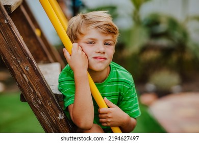 Cute Young Boy In Green Shirt And Black Shorts Is Playing On Back Yard Playground. Copy Space